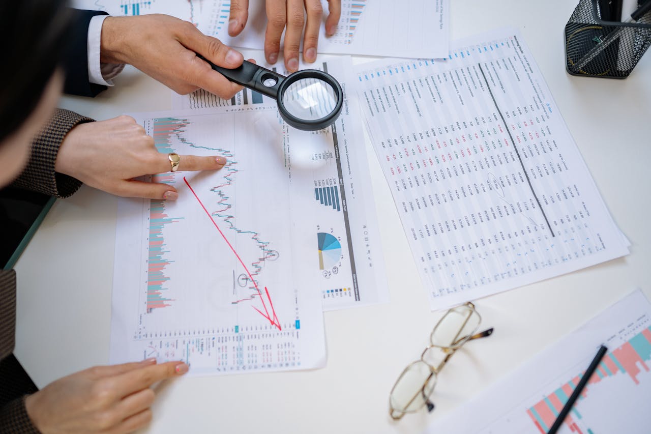 Business professionals examining financial documents with magnifying glass for detailed analysis.