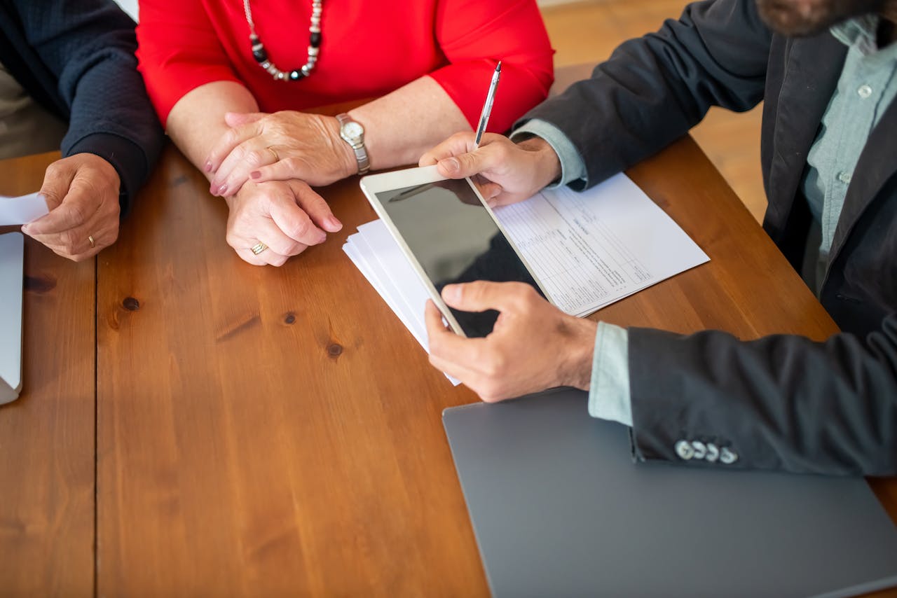 Business meeting at a wooden table with consultant reviewing documents and using a digital tablet.